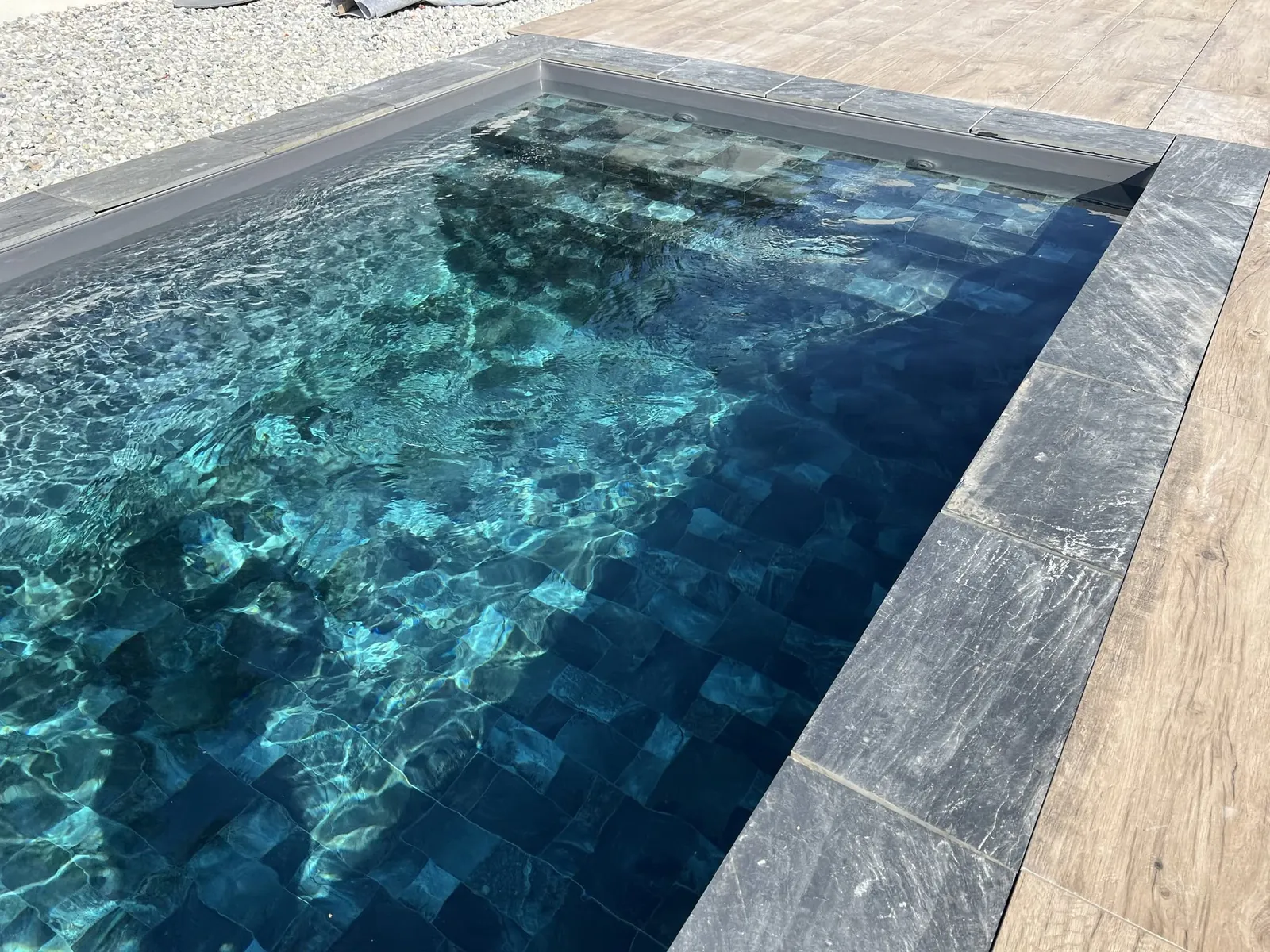 Fond de piscine avec membrane armée BWT Be BRANE 3D Surface Flagstone Jade, effet pierre bleu-vert profond vu sous l’eau sur une terrasse en bois