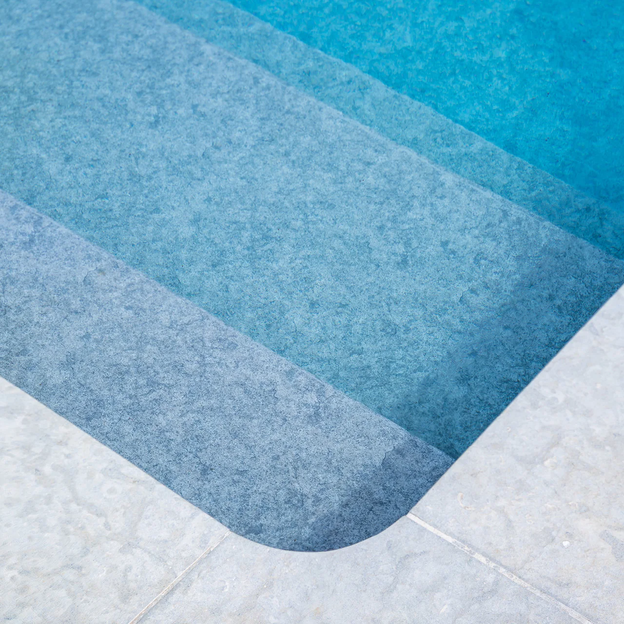 Marches de piscine avec membrane armée BWT Be BRANE 3D Surface Urban Grey, effet gris minéral et eau turquoise sur margelle en pierre claire